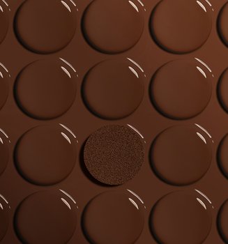 Artistic close-up of smooth, glossy drops of deep brown liquid foundation arranged in rows. In the center, a textured circular foundation cushion is saturated with a matching deep shade, highlighting foundation for deep skin tones.