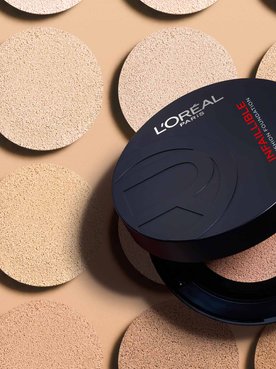 Image publicitaire du produit L'Oréal Paris Le Duo Serum. Le flacon luxueux, aux accents dorés et au corps transparent révélant deux formules distinctes (une claire et une ambrée), est présenté en diagonale. L'arrière-plan se compose de vagues onctueuses et satinées de textures blanches et dorées qui s'entrelacent, symbolisant la puissance et la richesse du mélange de sérums.