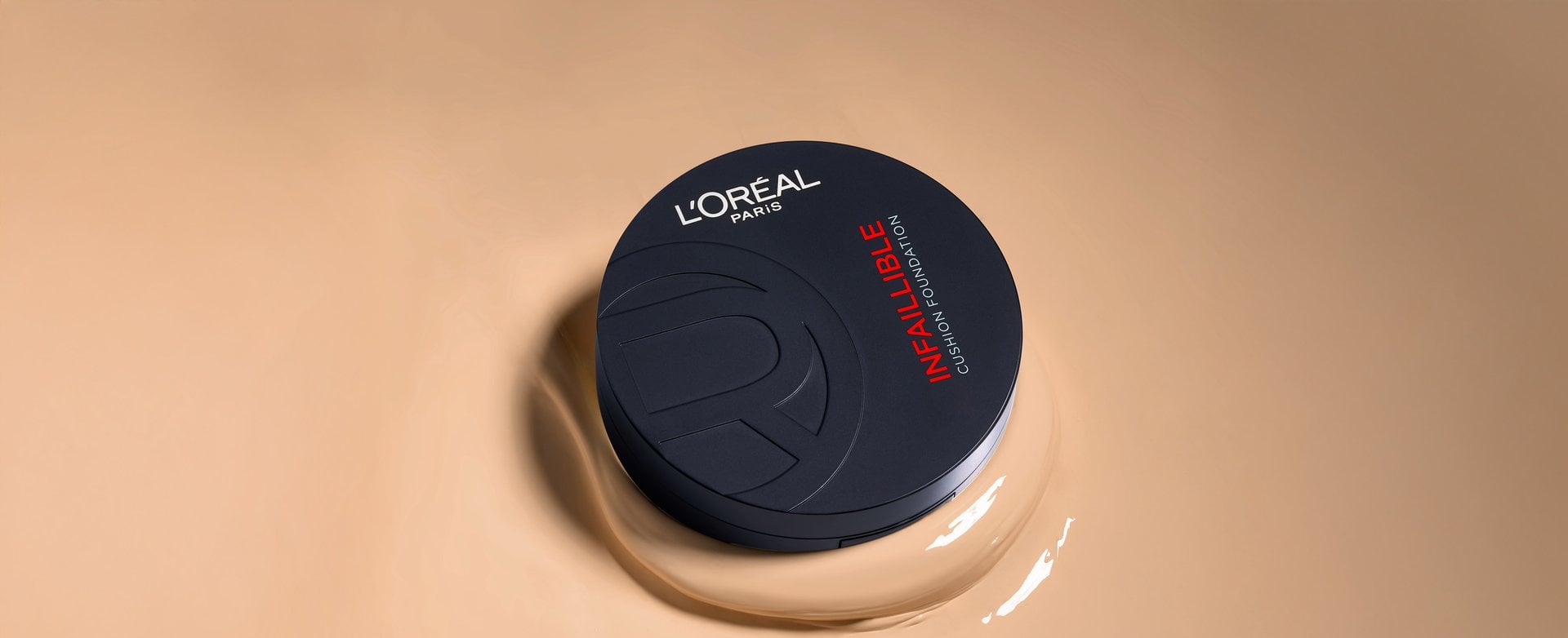 A vertical shot of a closed, matte black L'Oréal Paris Infallible Cushion Foundation compact. The product is resting on a large, smooth puddle of creamy liquid foundation in a light beige shade.