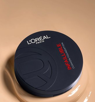A vertical shot of a closed, matte black L'Oréal Paris Infallible Cushion Foundation compact. The product is resting on a large, smooth puddle of creamy liquid foundation in a light beige shade.