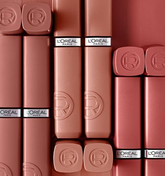 Plusieurs tubes de rouge à lèvres mat L'Oréal dans différentes teintes nude et rose, disposés verticalement côte à côte sur un fond mauve foncé uni.