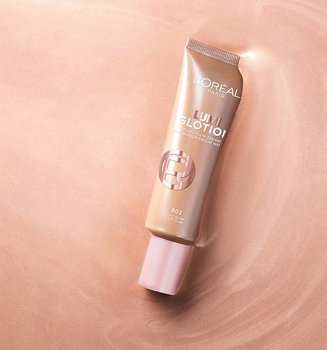Un tube d'enlumineur naturel Lumi Glotion de L'Oréal centré sur un fond liquide scintillant et iridescent de couleur or rose.