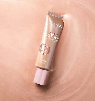 Un tube d'enlumineur naturel Lumi Glotion de L'Oréal centré sur un fond liquide scintillant et iridescent de couleur or rose.
