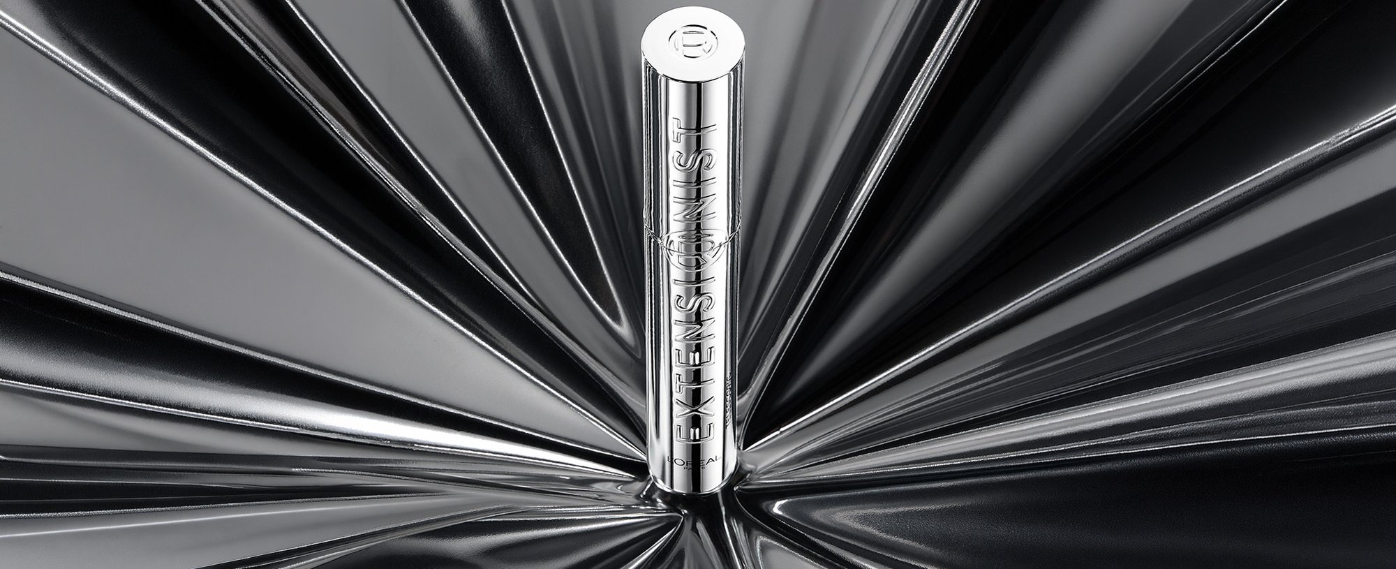 Un seul tube de mascara L'Oréal argenté posé verticalement au centre d'un fond argenté réfléchissant spectaculaire avec un motif lumineux radial.