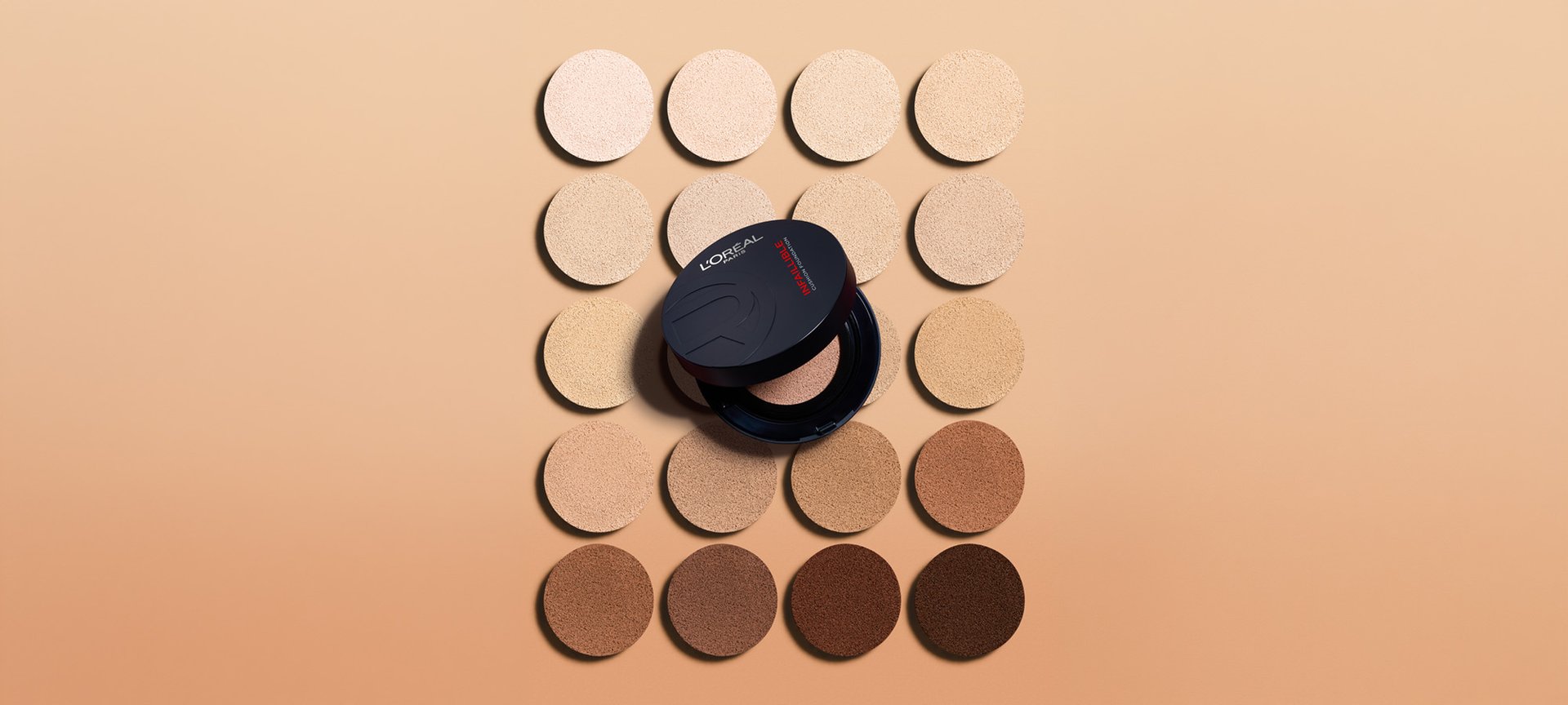A circular black L'Oréal compact placed in the center of a grid of foundation shade swatches, ranging from very fair to deep brown.
