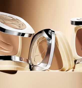 Four square L'Oréal foundation compacts in various shades ranging from light beige to deep tan, displayed on a warm golden-brown background.