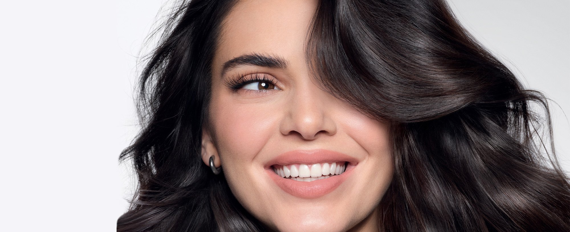 A young woman with long, dark, wavy hair smiles warmly at the camera.