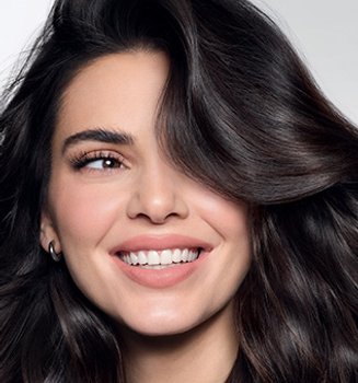A young woman with long, dark, wavy hair smiles warmly at the camera.