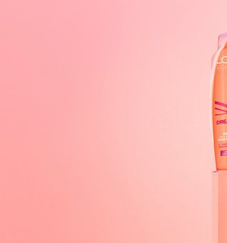 Flacons de shampooing et d'après-shampooing Dream Lengths de L'Oréal Paris dans un emballage pêche, posés sur des piédestaux roses translucides avec de la mousse blanche qui dégouline sur un fond rose doux.
