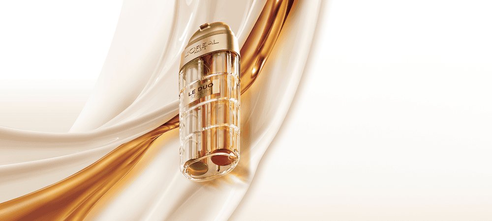 Image publicitaire du produit L'Oréal Paris Le Duo Serum. Le flacon luxueux, aux accents dorés et au corps transparent révélant deux formules distinctes (une claire et une ambrée), est présenté en diagonale. L'arrière-plan se compose de vagues onctueuses et satinées de textures blanches et dorées qui s'entrelacent, symbolisant la puissance et la richesse du mélange de sérums.