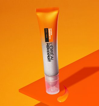 Tube orange de soin L'Oréal Men Expert Hydratation sur des formes géométriques oranges, avec une goutte de produit visible, sur un fond orange