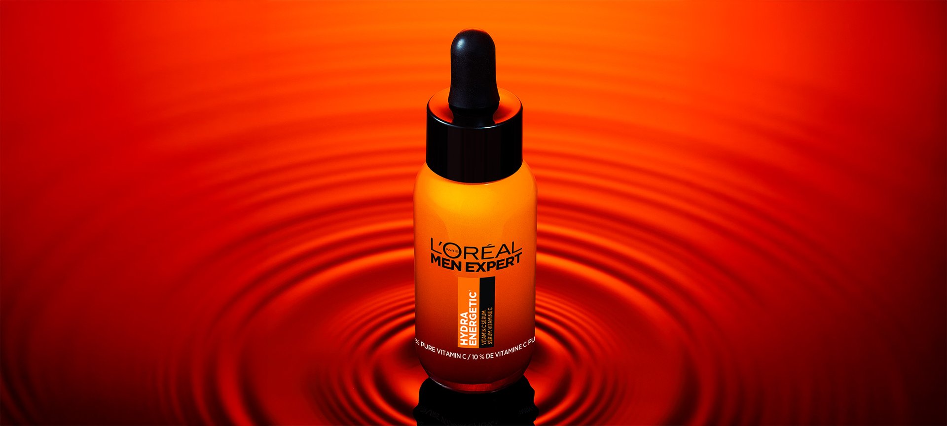 Orange bottle of L'Oréal Men Expert Hydratatic Serum with a black dropper, on a reflective red surface with ripples.