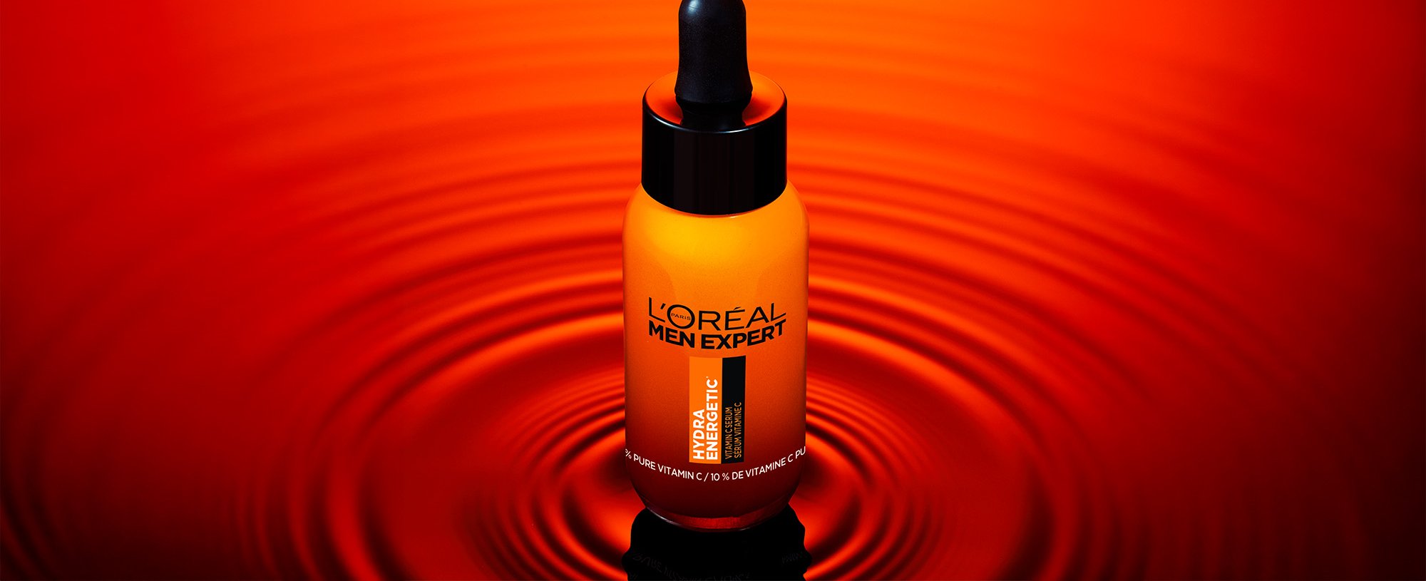 Orange bottle of L'Oréal Men Expert Hydratatic Serum with a black dropper, on a reflective red surface with ripples.