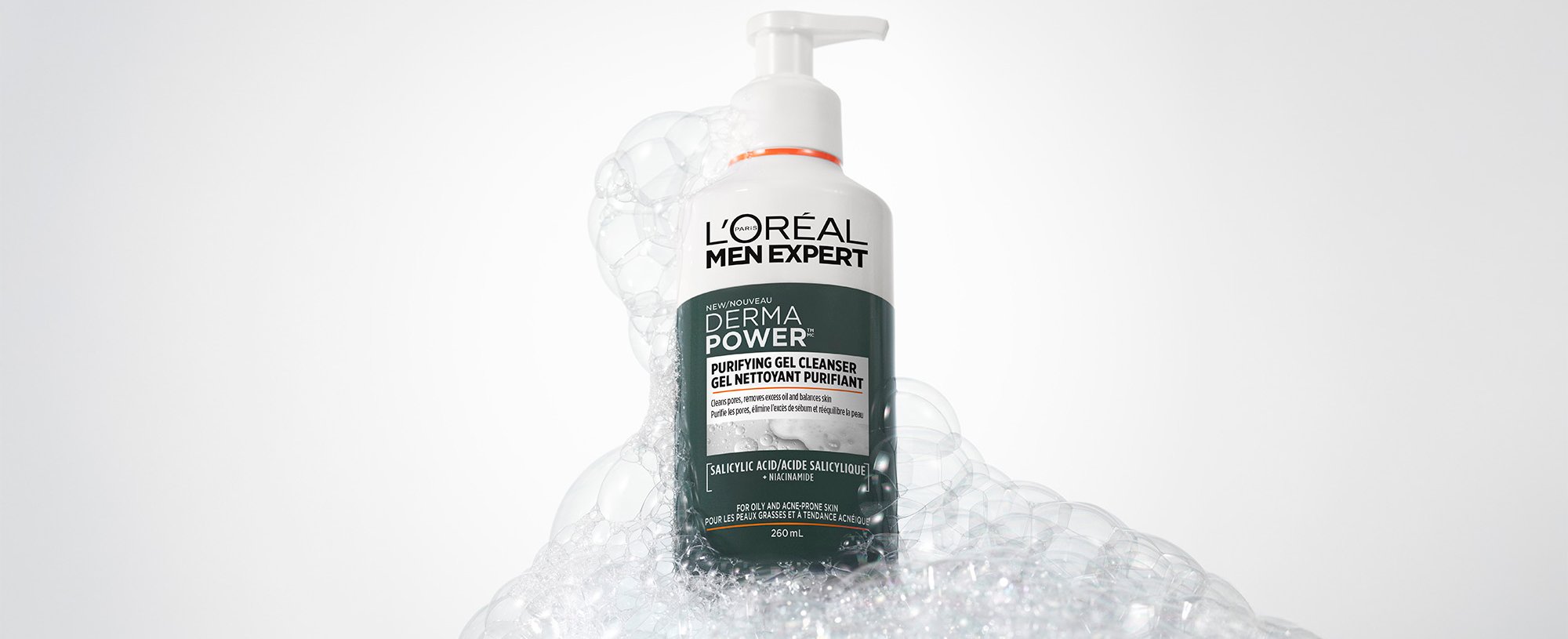 Flacon blanc de nettoyant purifiant L'Oréal Men Expert Derma Power avec pompe, entouré de bulles de savon blanches sur un fond gris.