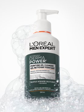 Flacon blanc de nettoyant purifiant L'Oréal Men Expert Derma Power avec pompe, entouré de bulles de savon blanches sur un fond gris.