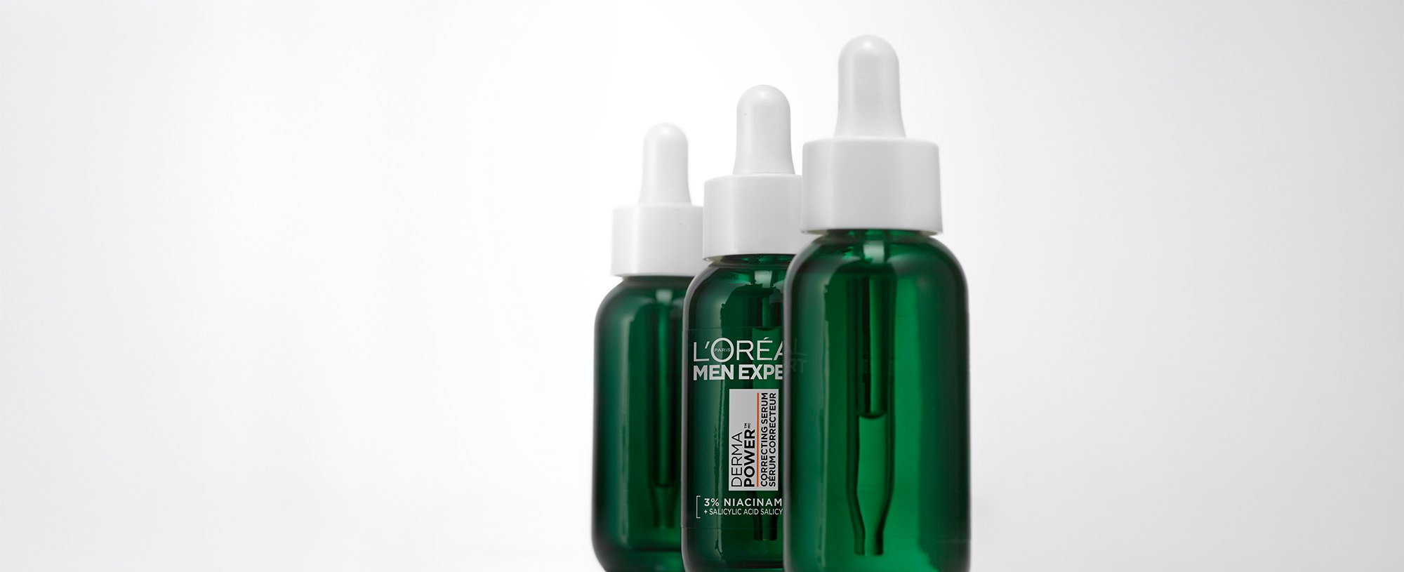 Trois flacons verts de sérum correcteur L'Oréal Men Expert Power Age avec pipettes, alignés sur un fond blanc.