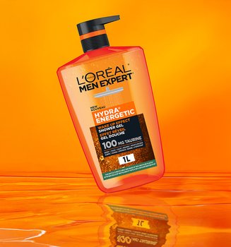 Flacon orange de gel douche L'Oréal Men Expert Hydra Energetic avec pompe noire, flottant sur un fond orange vif avec une surface réfléchissante.