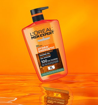 Orange bottle of L'Oréal Men Expert Hydra Energetic Shower Gel with a black pump, floating on a bright orange background with a reflective surface.