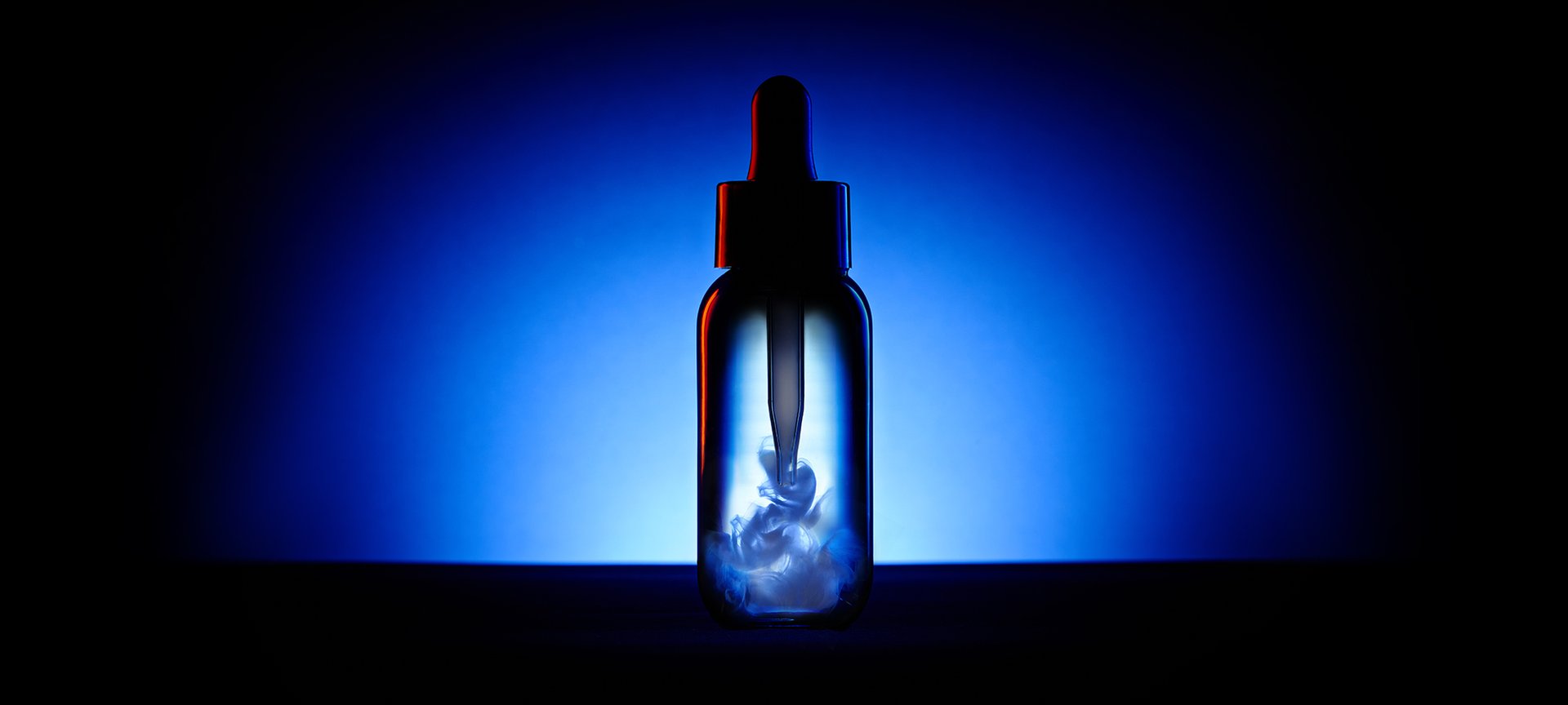 Dark bottle with a dropper containing white liquid swirling inside, set against a deep blue and black background.
