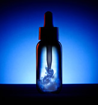 Flacon sombre avec pipette contenant un liquide blanc en suspension, sur un fond bleu et noir profond.