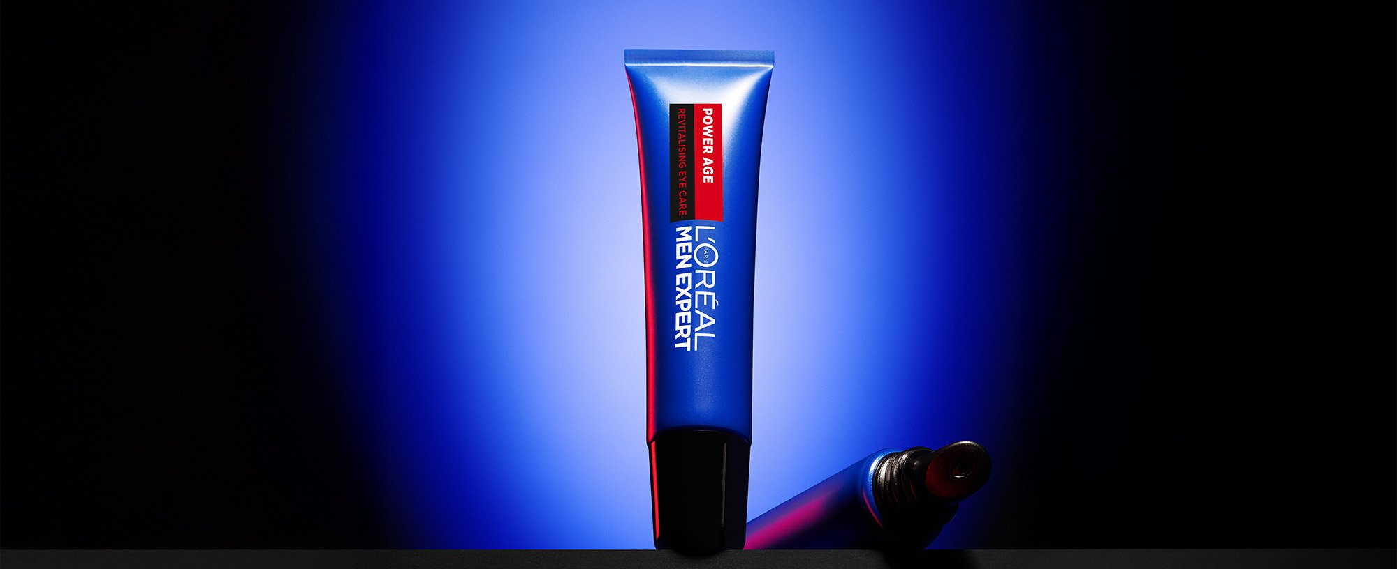Tube bleu de soin pour les yeux L'Oréal Men Expert Power Age Revitalising posé sur une surface sombre, avec un fond bleu.