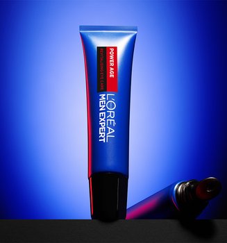 Tube bleu de soin pour les yeux L'Oréal Men Expert Power Age Revitalising posé sur une surface sombre, avec un fond bleu.