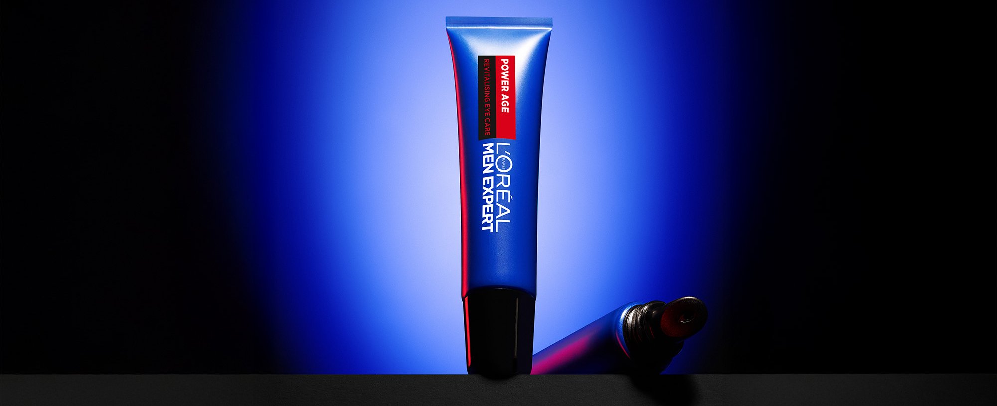 Blue tube of L'Oréal Men Expert Power Age Revitalising Eye Care lying on a dark surface, with a blue background.