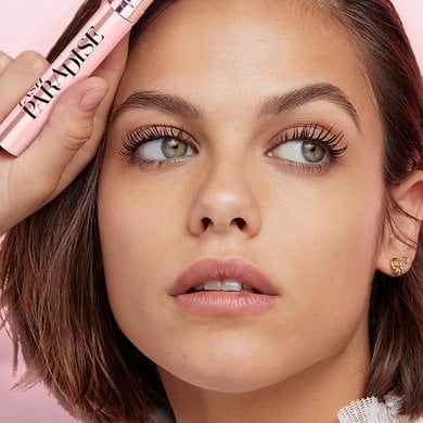 Une femme aux cheveux courts et bruns tient un mascara rose L'Oréal Lash Paradise, regardant vers le haut pour révéler ses cils magnifiquement déployés et volumineux.