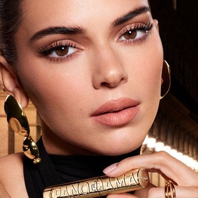 Kendall Jenner elegantly holds a gold Yves Saint Laurent Panorama mascara, highlighting her defined and extended eyelashes, symbolizing luxury and high-performance makeup.