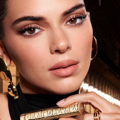 Kendall Jenner tient élégamment un mascara doré Yves Saint Laurent Panorama, mettant en valeur ses cils définis et allongés, symbolisant le maquillage de luxe et haute performance.