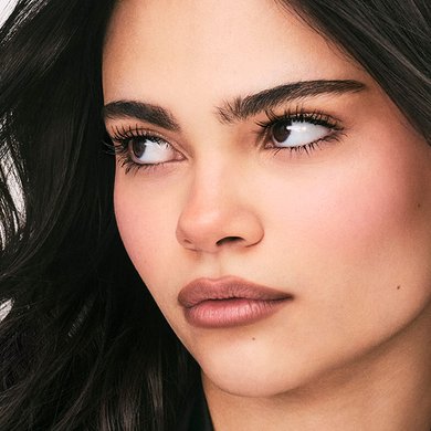 Une femme aux cheveux foncés et aux yeux saisissants regarde subtilement sur le côté, montrant ses cils naturellement rehaussés par le mascara, illustrant la définition et la beauté.