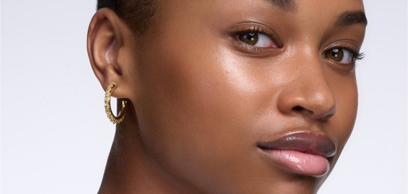 Gros plan d'une femme à la peau foncée et au teint éclatant, portant une boucle d'oreille anneau dorée.