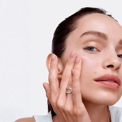 Gros plan d'une femme à la peau claire et au teint éclatant, touchant son visage.