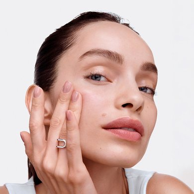Close-up of a woman with a fair skin tone and radiant, glowing skin, touching her face.