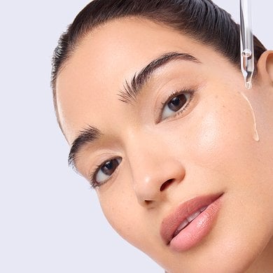 Gros plan d'une femme au teint éclatant alors qu'une goutte de liquide est appliquée sur sa joue à l'aide d'une pipette en verre.