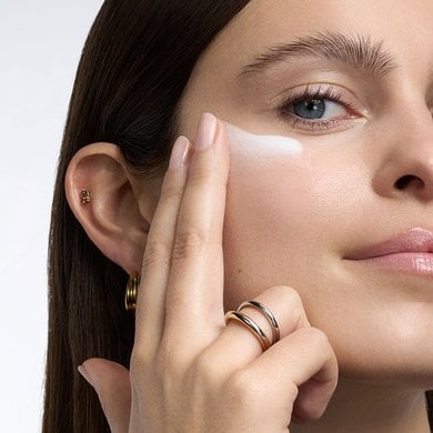 Gros plan d'une femme à la peau claire et au teint éclatant, appliquant une trace de crème ou de lotion blanche sur sa pommette avec ses doigts.