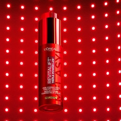 Studio shot of the red L'Oréal Paris Revitalift Triple Power LZR Melasyl serum bottle, centered against a vibrant red background featuring a structured grid pattern of small, glowing red LED-style lights.