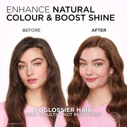 A split image displaying a woman's hair and facial expression before and after a treatment aimed at enhancing natural color and boosting shine. On the left, labeled "BEFORE," she has long, wavy, medium-brown hair that appears somewhat matte or less vibrant, and her expression is neutral. On the right, labeled "AFTER," her hair is a richer, warmer shade of medium brown, with a clear, glossy sheen and more defined waves. She is smiling gently, and her complexion is fresh with a subtle pink flush. The text at the top reads: "ENHANCE NATURAL COLOUR & BOOST SHINE." Below the images, it states: "3X GLOSSIER HAIR*" and "REAL RESULTS - NOT RETOUCHED," with an asterisk indicating "*INSTRUMENTAL TEST."
