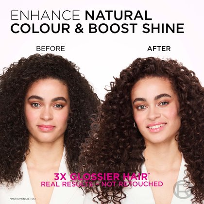 A split image showing a woman with voluminous, curly hair before and after a treatment designed to enhance natural color and boost shine. On the left, labeled "BEFORE," her hair is a dark brown, appearing somewhat matte, and her expression is neutral. On the right, labeled "AFTER," her hair is a richer, darker brown with a noticeable glossy finish, and her curls appear more vibrant and defined. She is smiling broadly. The text at the top reads: "ENHANCE NATURAL COLOUR & BOOST SHINE." Below the images, it states: "3X GLOSSIER HAIR*" and "REAL RESULTS - NOT RETOUCHED," with an asterisk indicating "*INSTRUMENTAL TEST."