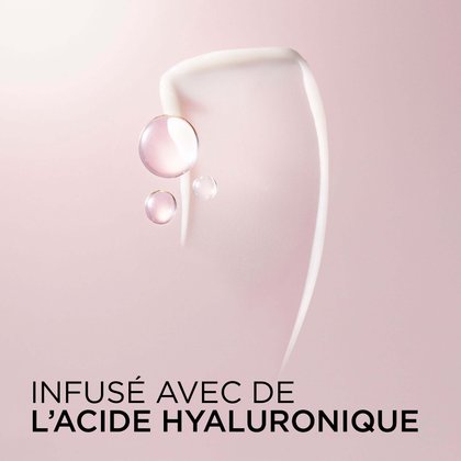 Gros plan artistique d'un tourbillon de crème revitalisante blanche avec des sphères translucides roses représentant l'acide hyaluronique sur fond rose. Texte : Enrichi en acide hyaluronique.