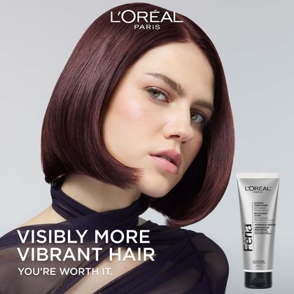 L'Oréal Paris campaign image featuring a model with glossy, deep burgundy-red hair in a sleek bob cut, looking directly at the camera. Text reads "Visibly More Vibrant Hair – You're Worth It." The Féria Ultimate Conditioner silver tube is shown in the bottom right corner. L'Oréal Paris logo at the top.