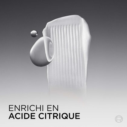 Gros plan en studio sur fond dégradé sombre montrant une texture épaisse de revitalisant blanc avec deux gouttes liquides argentées et brillantes à côté, représentant l'ingrédient actif acide citrique. Le texte en bas indique : « Enrichi en acide citrique. »