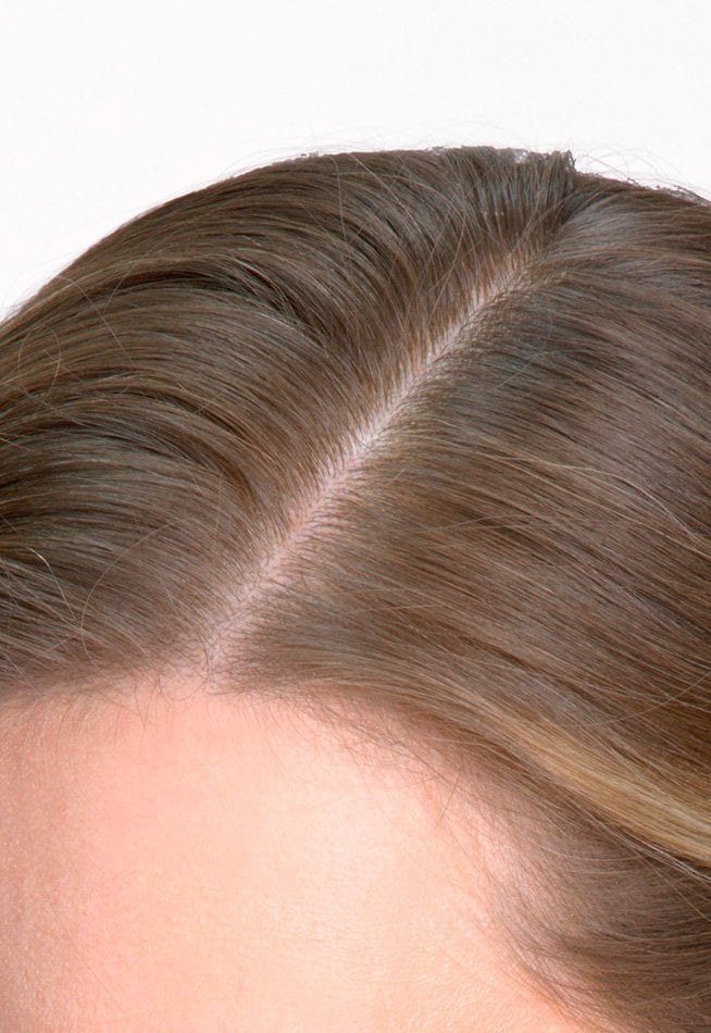 Close-up of the same hair after applying a root concealer spray; the grey hair is gone, replaced by a natural and uniform brown color.