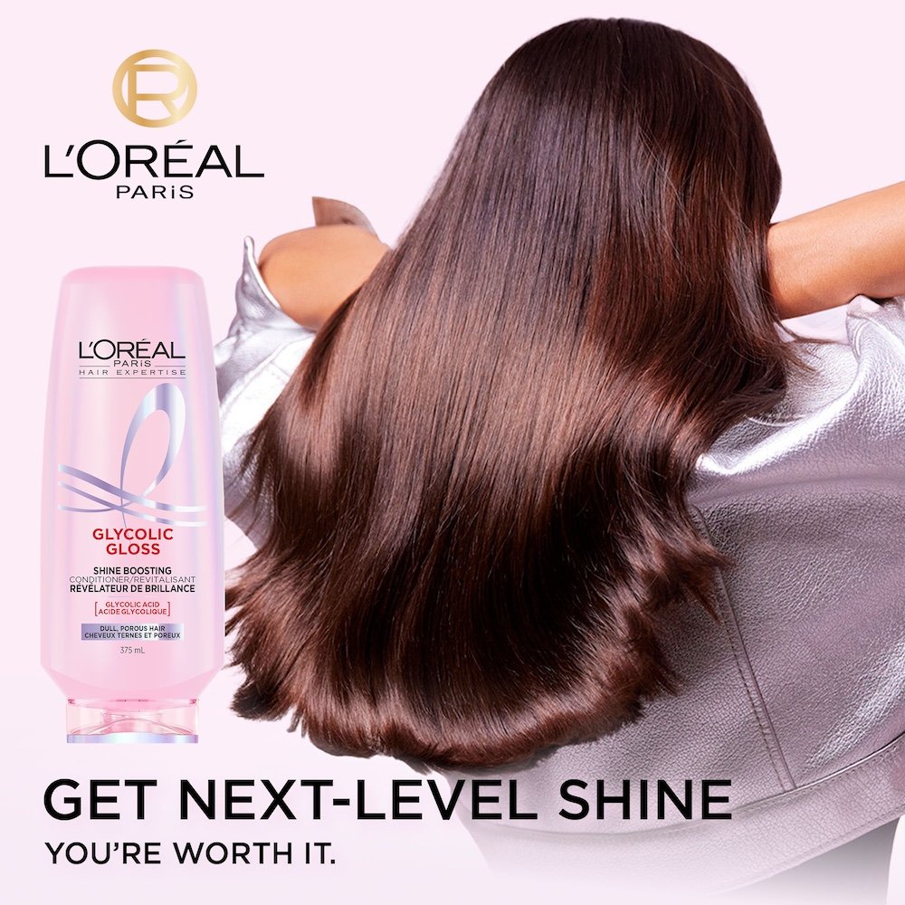 A L'Oréal Paris Glycolic Gloss Shine Boosting Conditioner bottle (375 mL) stands next to a model from behind, showcasing her long, dark, incredibly shiny, and smooth hair. The text "GET NEXT-LEVEL SHINE YOU'RE WORTH IT." is visible at the bottom.