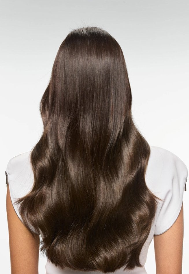  Back view of a person with long, shiny, wavy dark brown hair, against a white background.