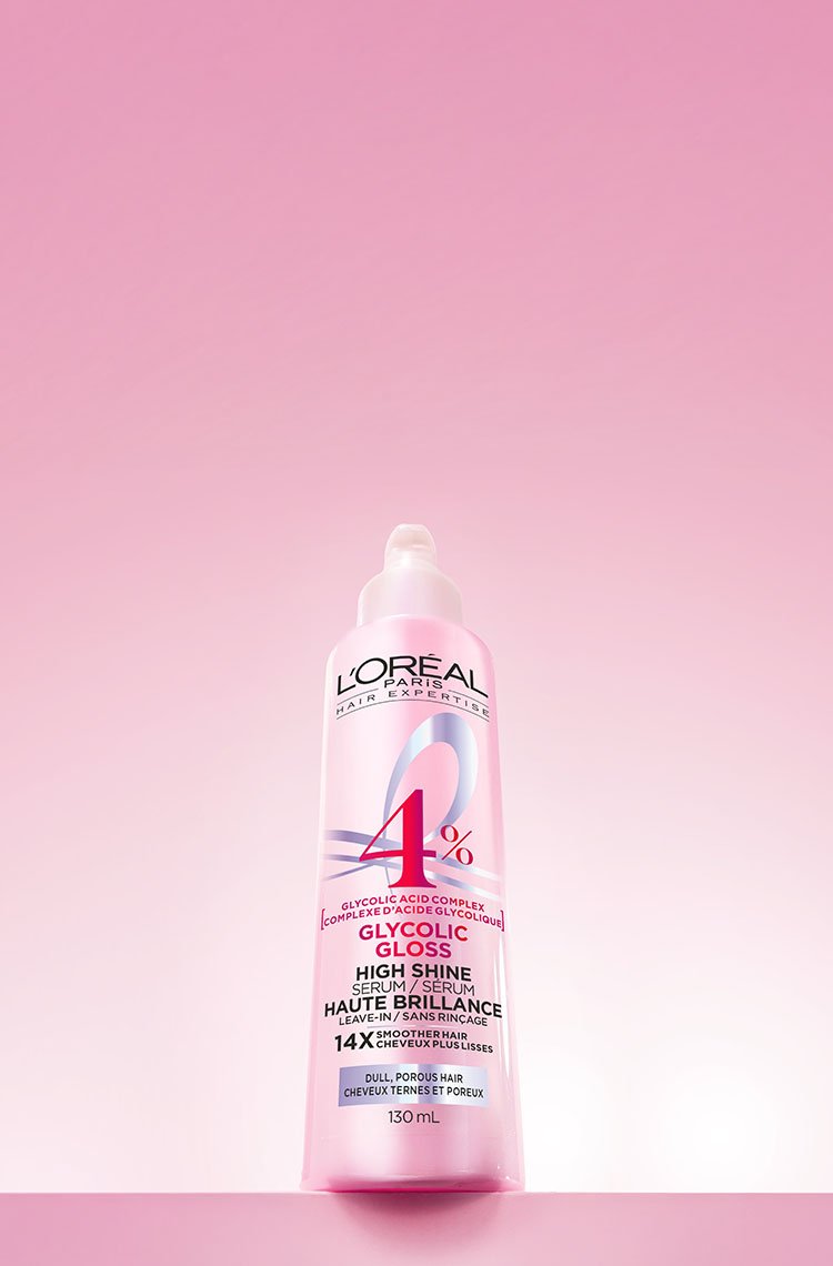 A L'Oréal Glycolic Gloss High Shine treatment bottle with 14% glycolic complex, on a pink background with luminous reflections.