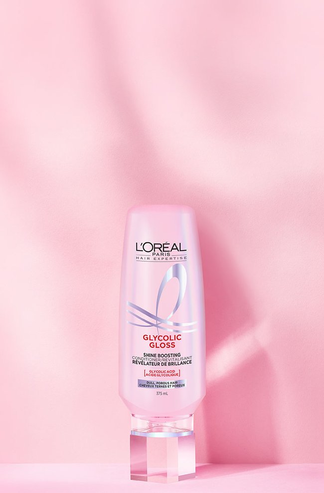 A L'Oréal Glycolic Gloss conditioner pump bottle, on a pink background with radial luminous lines.