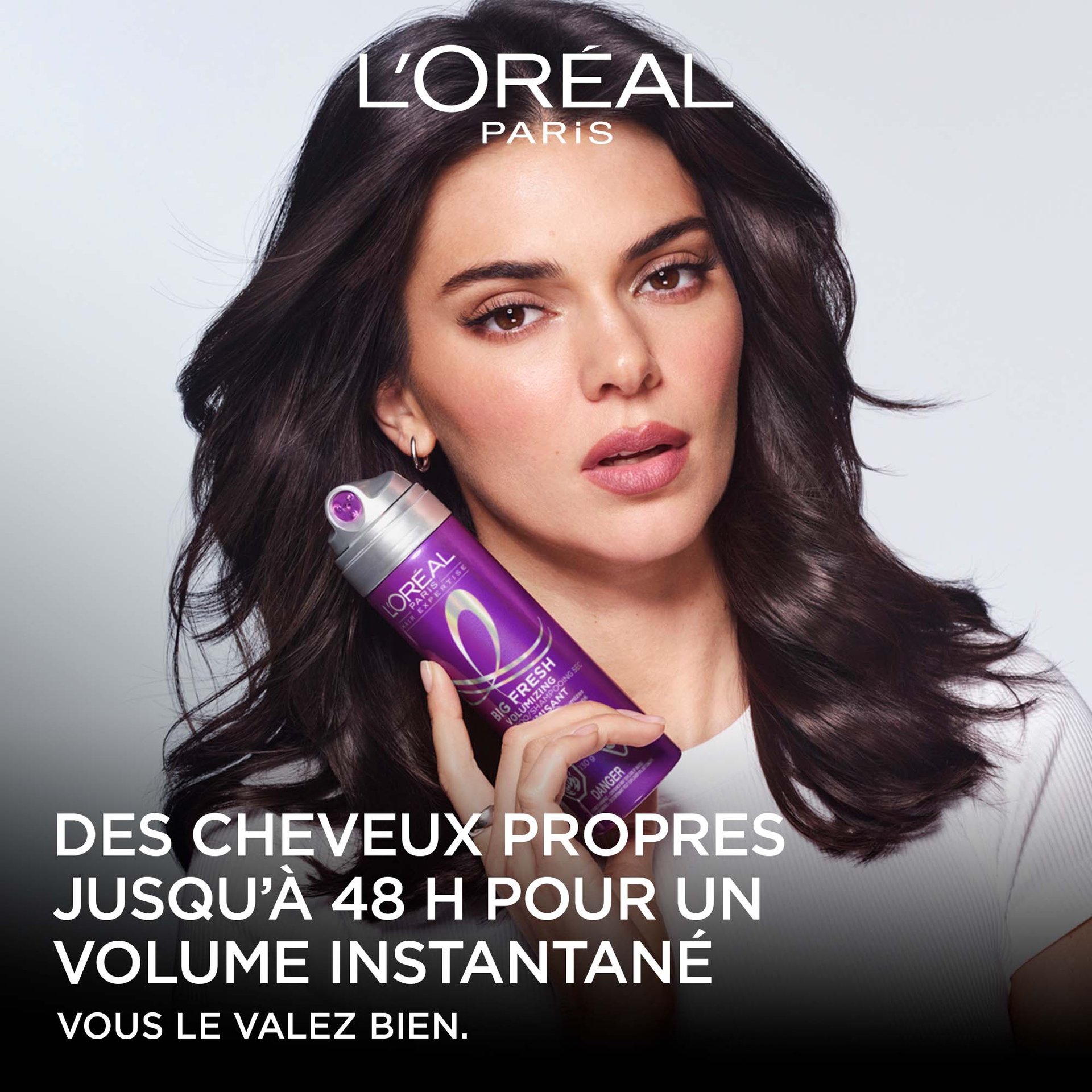 Vue de face de l'égérie de L'Oréal Paris, Kendall Jenner, avec des cheveux foncés volumineux, tenant le flacon de shampooing sec volumisant violet Big Fresh. Le texte indique : « Purifie les cheveux jusqu'à 48 h. Transformation instantanée du volume. »