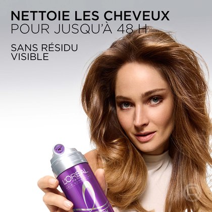 Une femme souriante aux cheveux bruns volumineux tenant le shampooing sec violet en spray. Le texte indique : « Purifie les cheveux jusqu'à 48 h. Sans résidu visible. »