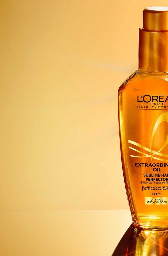 Deux bouteilles de L'Oréal Paris Hair Expertise Huile Extraordinaire Sublime Cheveux Parfaits, l'une avec un reflet lumineux, sur un fond doré